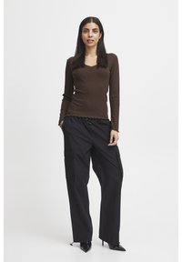 Brauner, gerippter Langarm-Oberteil mit V-Ausschnitt, kombiniert mit schwarzen Cargo-Hosen mit Seitentaschen. Schwarze spitze Absatzschuhe runden den Look ab.