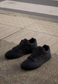 Black athletic shoes with a smooth leather-like material. Features laces, a prominent "N" logo, and textured rubber soles.