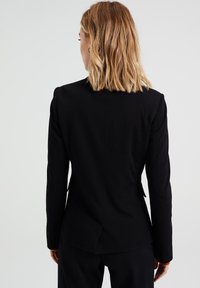 Svart skräddarsydd kavaj med slag, enkel ryggslits och långa ärmar. Slätt tyg med en åtsittande design och subtila sömnadsdetaljer.