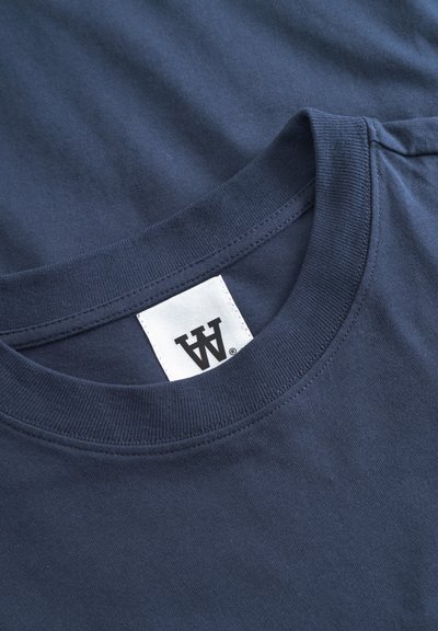 T-shirt en coton bleu marine avec col rond et texture lisse. Présente une étiquette avec un logo sur un fond blanc uni.