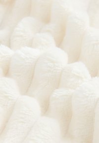 Tissu en peluche crème texturé avec motifs ondulés en relief. Surface douce et moelleuse qui améliore l'expérience tactile, adapté pour les couvertures ou les revêtements.