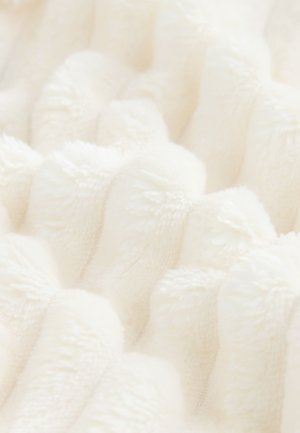 Strukturiertes cremefarbenes Plüschgewebe mit erhabenen, wellenförmigen Mustern. Weiche, flauschige Oberfläche für ein angenehmes haptisches Erlebnis, geeignet für Decken oder Polster.