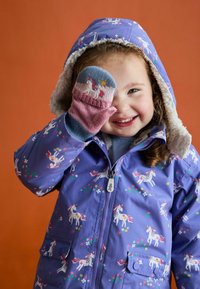 Lila wasserdichte Jacke mit Einhornmuster, gefütterter Kapuze aus Kunstpelz und Fronttaschen. Kind trägt bunte, gestrickte Handschuhe mit Tiermotiv.