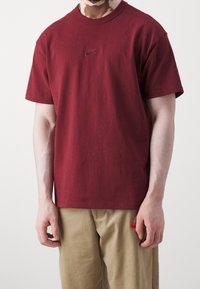 T-shirt in cotone marrone scuro con un piccolo logo Nike ricamato sul petto. Maniche corte e collo a giroclassico.