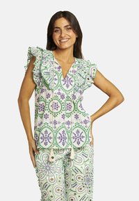 Blusa blanca con patrones florales verdes y morados, mangas con volantes y escote en V. Combinada con pantalones a juego con patrones similares.
