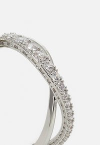 Silverring med två böjda band som är sammanlänkade, prydd med klara, rundslipade stenar som är infattade i en polerad metallram.