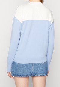 Ljusblå stickad tröja med vit axelparti och spetsstruktur vid axlarna. Har långa ärmar och ribbad nederkant. Matchad med en denimkjol.