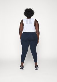 Top blanco sin mangas con panel de malla, combinado con leggins azul marino y zapatillas negras. Los leggins son ajustados y tienen una textura suave.