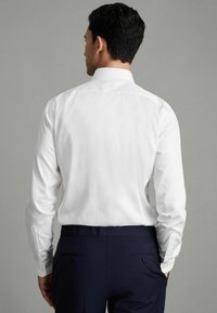 Weißes Langarmhemd mit umgelegtem Kragen, schlichte Textur und dazu passende navyfarbene Hose mit glatter Oberfläche und zwei Gesäßtaschen.