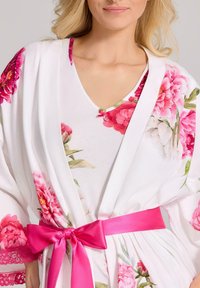 Kwiatowy kimono w kolorze białym, z różowymi wzorami piwonii, głębokim dekoltem w kształcie V oraz różowym satynowym paskiem zawiązanym w pasie.