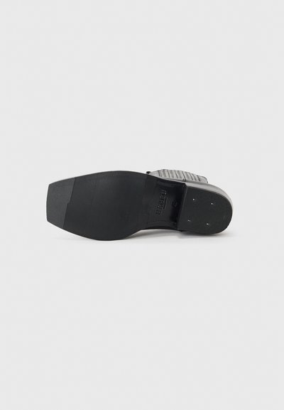Suola di scarpe nera in gomma testurizzata per una maggiore aderenza, con un design piatto e motivi lineari. Costruzione resistente con accenti in metallo.