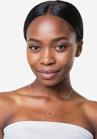 Silverhalsband med en cirkulär berlock som har små klara stenar, bärs mot en bar nyckelben på en modell med slät hud.