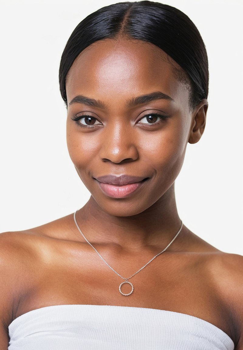 Silverhalsband med en cirkulär berlock som har små klara stenar, bärs mot en bar nyckelben på en modell med slät hud.