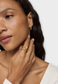 Gold hoop earring and layered ring showcasing a bear charm, worn on a hand. Smooth texture and simple design. Natural skin tone and light polish on nails.