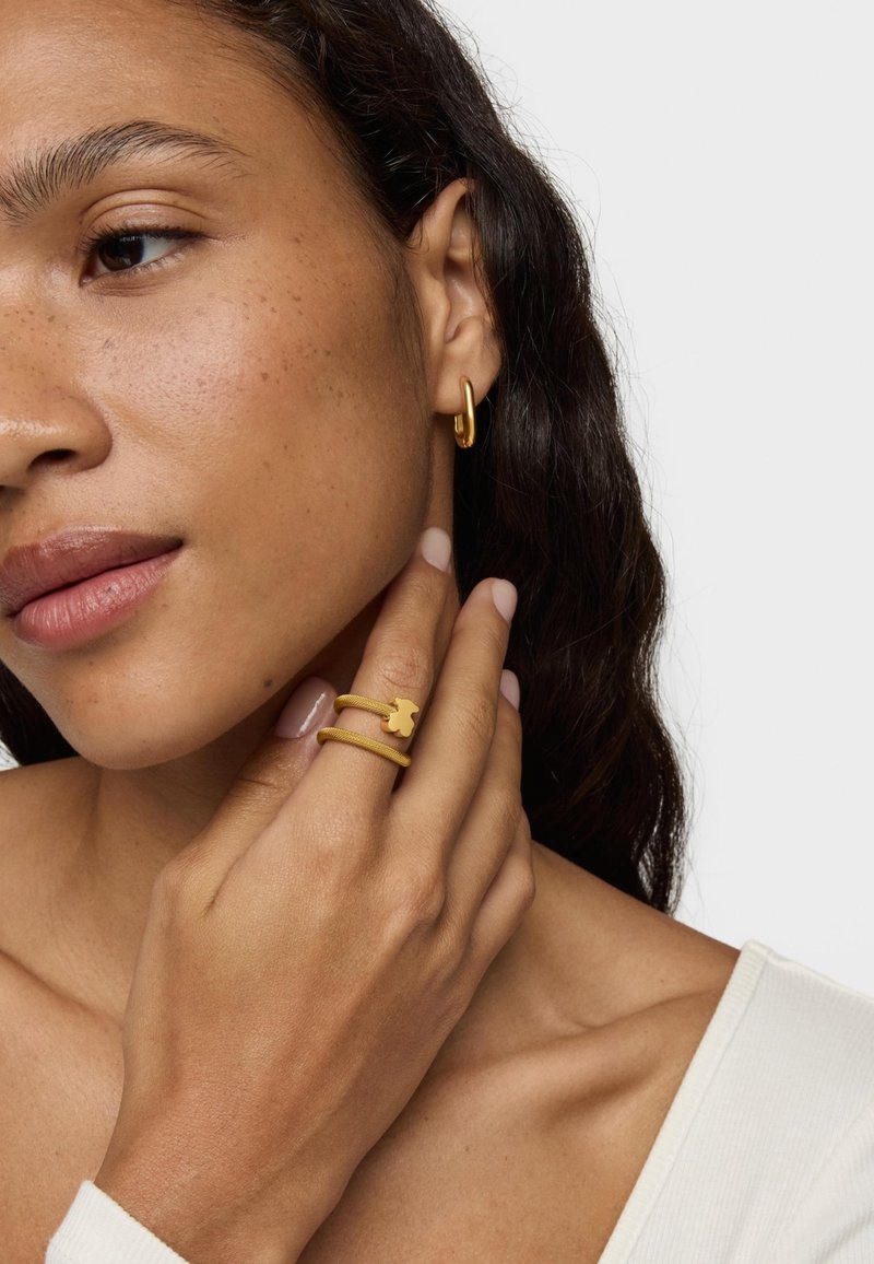 Gold hoop earring and layered ring showcasing a bear charm, worn on a hand. Smooth texture and simple design. Natural skin tone and light polish on nails.