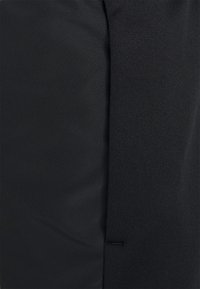 Gros plan d'un tissu noir avec deux textures différentes reliées par une couture, montrant des sections de matériau lisses et légèrement côtelées.