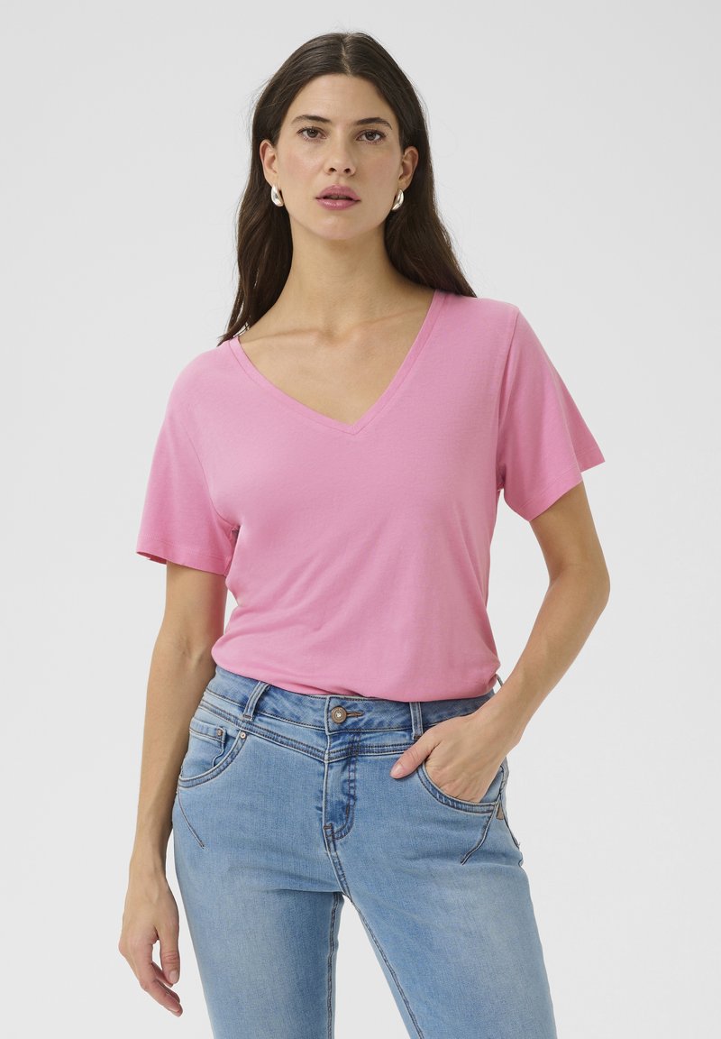 Rózsaszín V nyakú póló puha anyagból, rövid ujjú, világoskék farmerral párosítva. A póló laza szabású és sima tapintású.