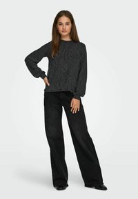 Maglione nero a maniche lunghe con design a coste, abbinato a jeans neri a gamba larga e vita alta; scarpe nere con punta affilata.