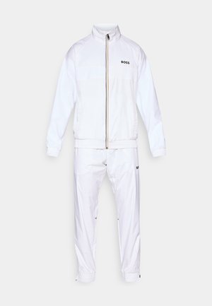 Tuta bianca realizzata in materiale morbido e leggero. Presenta una giacca con zip e colletto alto, con polsini elasticizzati, e pantaloni abbinati con vita elastica.
