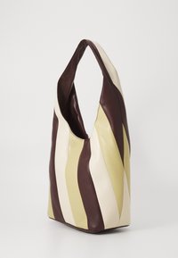 Μαλακή δερμάτινη τσάντα tote με φαρδύ χερούλι, διαθέτοντας κατακόρυφες ρίγες σε κρέμα, μπεζ και σκούρο καφέ χρώμα πάνω σε απλό φόντο.