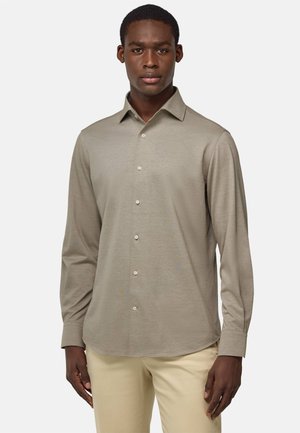 Long-sleeve, beige shirt with a button-up front and collar. Smooth texture with a tapered fit. Paired with light-colored trousers.