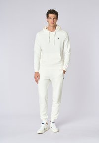 Felpa bianca con tasca frontale e cordini, abbinata a pantaloni jogger bianchi coordinati. Presenta un piccolo logo navy sul petto e sui pantaloni.