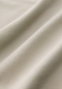 Beige texturerat tyg med synligt vävmönster, som har mjuka veck och subtil glans, vilket framhäver dess släta yta och böjlighet.