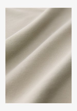 Beżowa tkanina o wyraźnym wzorze splotu, z miękkimi fałdami i subtelnym połyskiem, podkreślająca gładką powierzchnię i elastyczność.