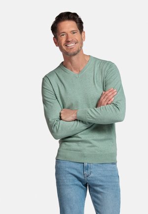 Groene, lichte trui met een V-hals en lange mouwen. De stof heeft een zachte, gladde textuur. Gepaard met lichtblauwe spijkerbroek.