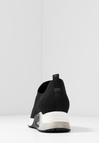 Baskets tricotées noires avec semelle blanche et grise, coussin d'air visible et languette à l'arrière, vues de dos sur une surface blanche.