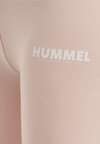 Różowe legginsy sportowe o gładkiej fakturze i dopasowanym kroju. Zawierają napis "HUMMEL" w białym kolorze oraz "SPORTSWEAR SINCE 1923" poniżej.
