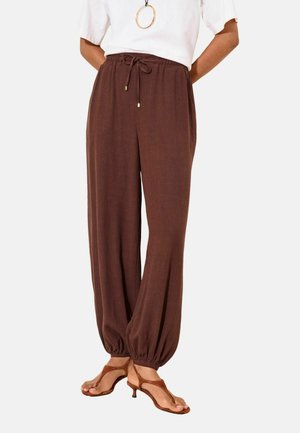 Brown loose-fit trousers with elastic cuffs, drawstring waist, worn with brown heeled sandals and a white top.