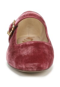 Scarpa piatta in velluto bordeaux con punta arrotondata, decorata con una fibbia dorata circolare sul lato, caratterizzata da una texture liscia e un design minimale.