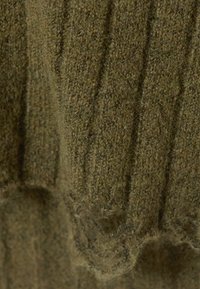 Gros plan sur un tissu tricoté en olive texturé avec un motif de surface côtelé et duveteux.