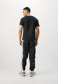 Black athletic t-shirt with blue accents and a rounded neckline, paired with black and grey tapered track pants, designed for comfort and mobility.