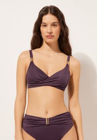 Lila bikini med en snurrad design. Toppen har justerbara band och guldaccessoarer. Botten delarna har en rynkad struktur med en central detalj.