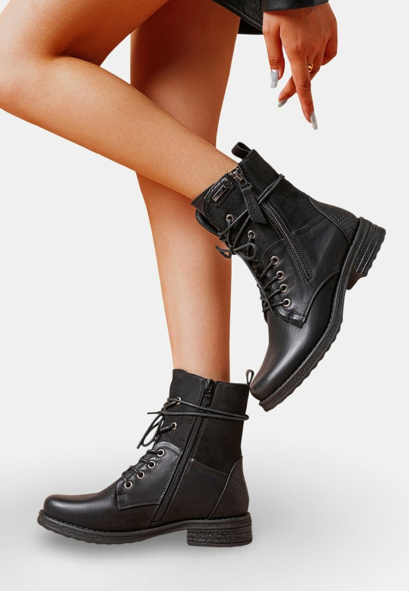 Bottines noires avec une finition en cuir lisse et en daim, présentant des lacets et une fermeture éclair, un bout rond et une semelle en caoutchouc texturée.