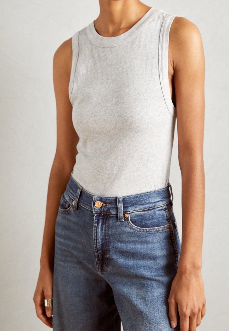 Top gris sin mangas hecho de algodón suave. Combinado con jeans de mezclilla azul de cintura alta con acentos de botones dorados y una textura ligeramente desgastada.