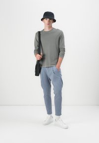 Chemise grise à manches longues, pantalon tapered bleu clair, chapeau seau noir, baskets blanches et sac messager noir. Design simple et décontracté.