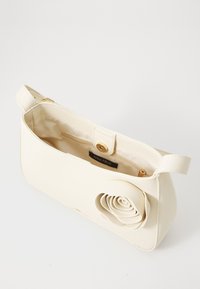 Bolso de mano de imitación cuero blanco con un adorno en forma de rosa, cierre superior con cremallera y un solo asa. El interior cuenta con un forro de tela.