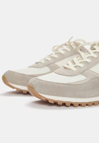 Világosszürke velúr felsőrésszel, fehér részletekkel és mintás gumitalppal rendelkező sneakers. Kerek fűzőkkel és karcsú dizájnnal bír.