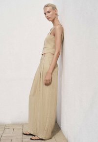 Beige linneoutfit med en kortad linne och flödande vidbyxor. Slät textur med minimalistisk design och tunna band.