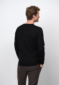 Schwarzer, langärmeliger Pullover aus Strickmaterial. Verfügt über einen klassischen Rundhalsausschnitt und eine schlanke Passform, mit minimalen Details auf der Rückseite.