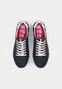 Granatowe płócienne trampki z białymi sznurowadłami, okrągłym noskiem i czerwonym wkładem pokazującym logo "Tommy Hilfiger". Posiadają paskowane akcenty na kołnierzu.