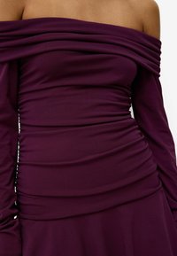 Dark purple off-the-shoulder dress made of stretchy fabric with gathered texture along the bodice and long sleeves. Smooth finish.