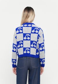 Person wearing a blue and gray checkered sweater with cherry patterns, paired with dark blue pants, viewed from the back.