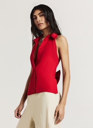 Blouse sans manches rouge avec un col, dotée de boutons sur le devant et d'un détail noué au dos, en tissu lisse et au design ajusté.