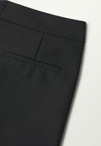 Pantalons noirs ajustés avec une texture lisse et une poche arrière unique ornée d'un détail de couture subtil à la taille. Design minimaliste.