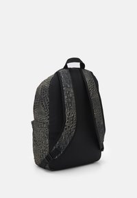 Svart ryggsäck med texturerat krokodilmönster på remmarna, mörk kropp och ett bärhandtag. Utformad med justerbara sidoremmar för stöd.