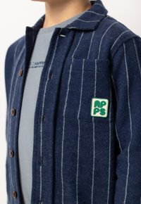 Navy wollen flanellen overhemd met verticale witte strepen, knoopsluiting, borstzak en een groen patchlogo op de zak.
